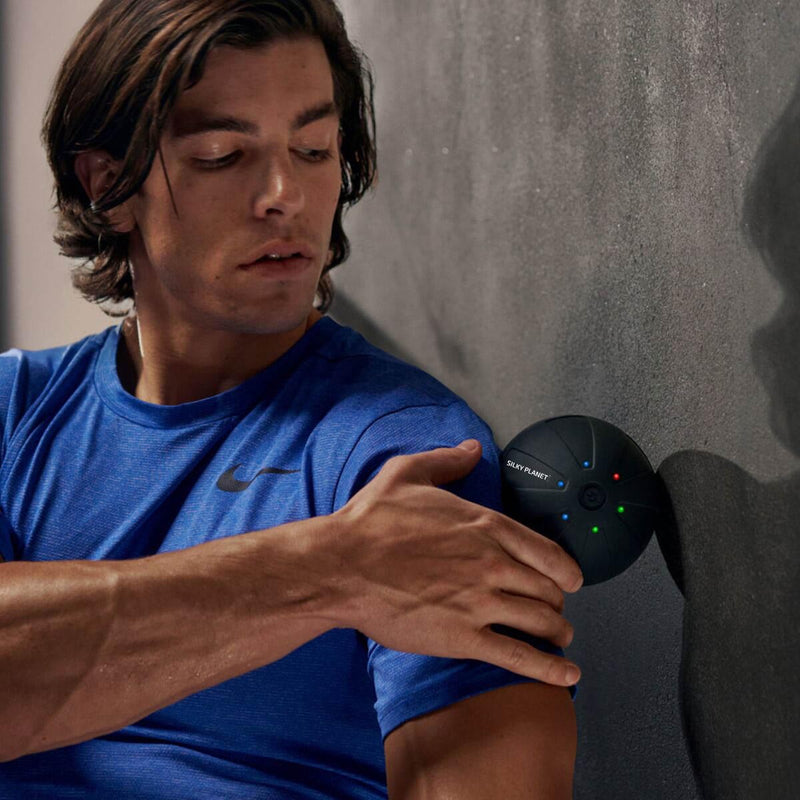 En man använder Silky Planets massageboll för att massera axeln mot en vägg.